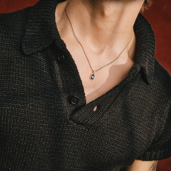 Person wearing a black knitted cardigan with a necklace featuring a green gemstone.