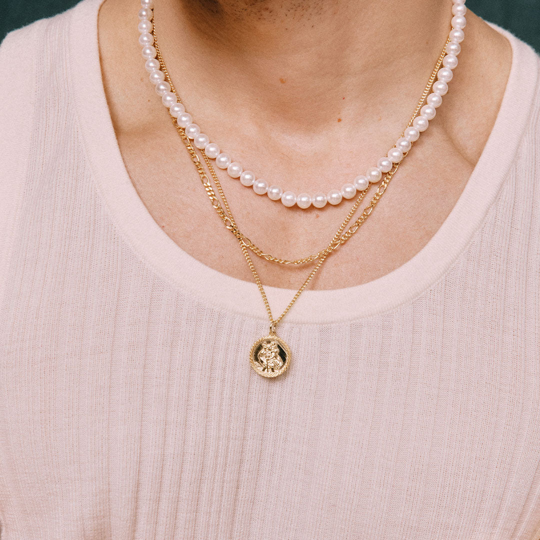 Close-up of a person wearing multiple necklaces with a gold pendant on a white top