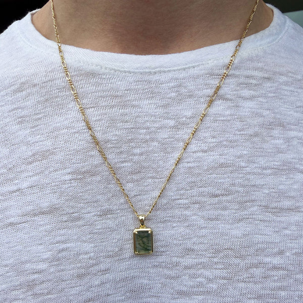 Gold necklace with a green pendant on a white shirt