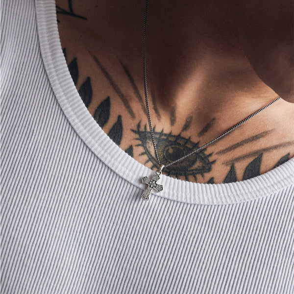 Model with chest tattoo wears white ribbed top under a Silver necklace with cross pendant