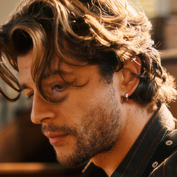Close-up of a person with wavy hair and a black shirt, with a blurred background.