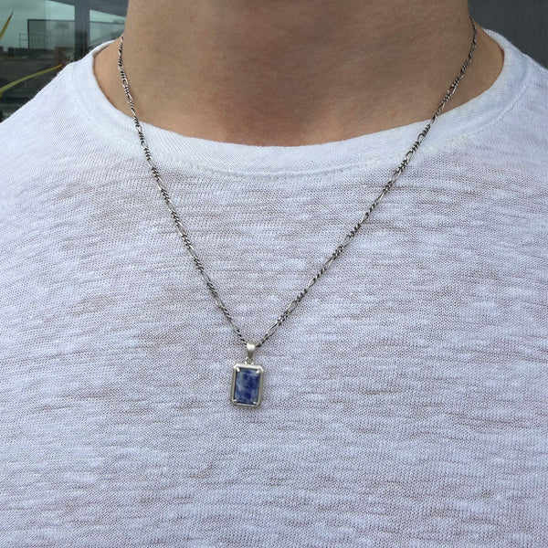 Person wearing a necklace with a blue pendant on a plain background