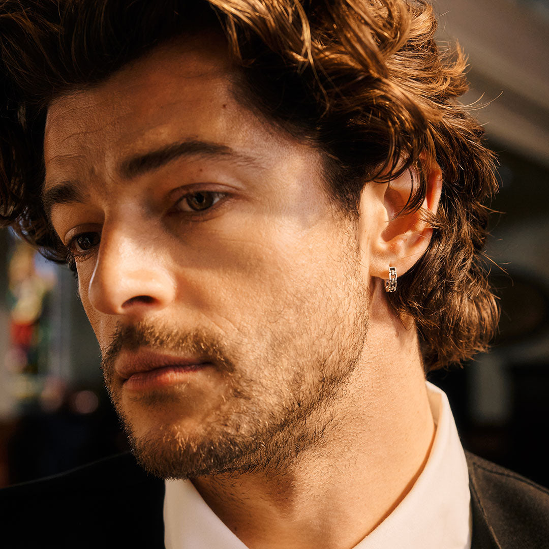 Close-up of a man with styled hair and earring against a blurred background