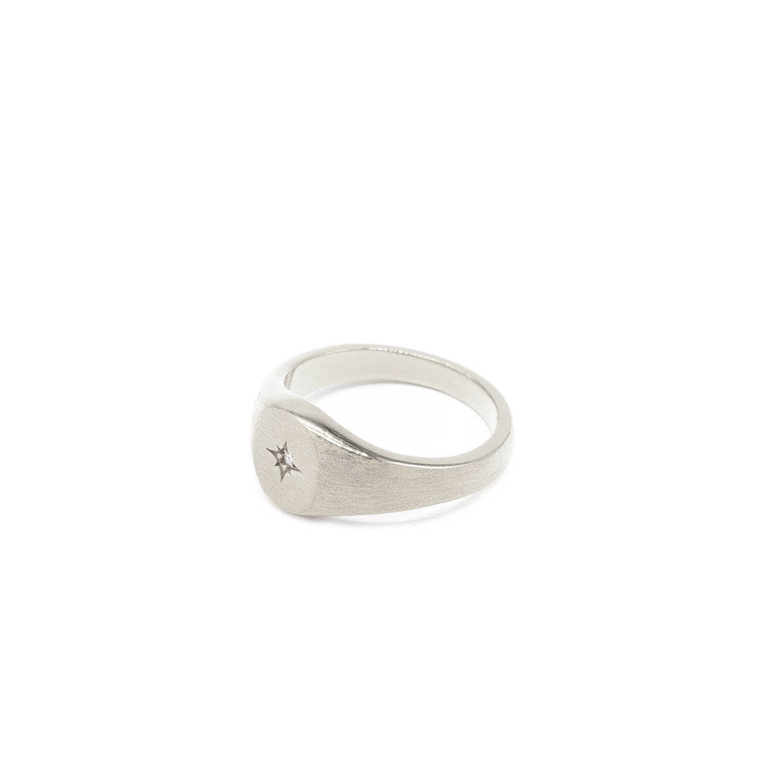 Silver oval signet ring with a star setting and diamond in the centre with a heavy brushed finish on a white background