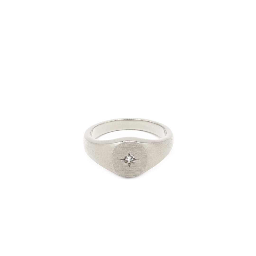 Silver oval signet ring with a star setting and diamond in the centre with a heavy brushed finish on a white background