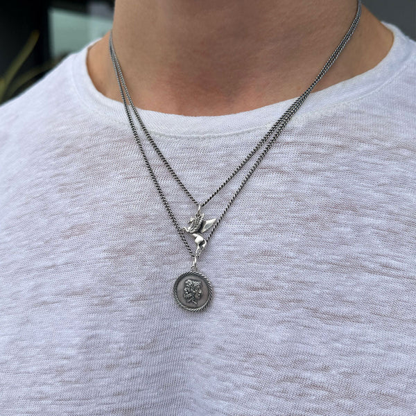 Two silver necklaces with pendants on a light gray shirt
