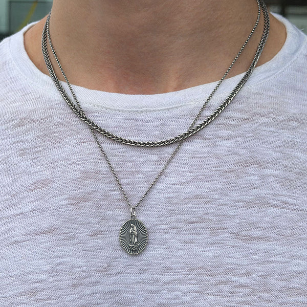 Close-up of a person wearing two silver necklaces with a pendant on a white shirt.
