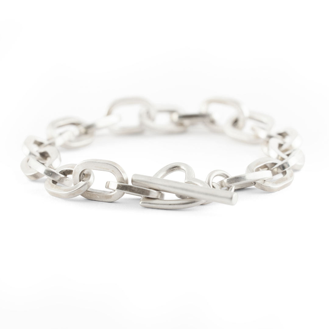 Silver thick chain bracelet with oval links and a t bar closing function on a white background