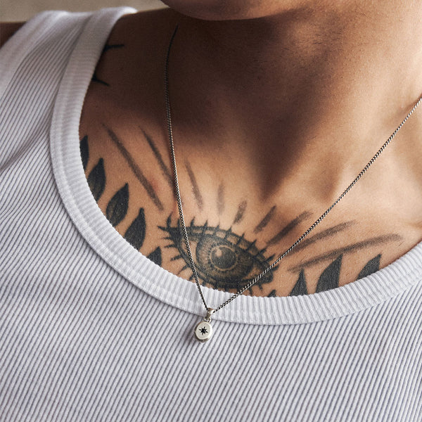 Male model with tattoo'ed chest wears a white ribbed vest with a Silver pendant necklace - Serge DeNimes