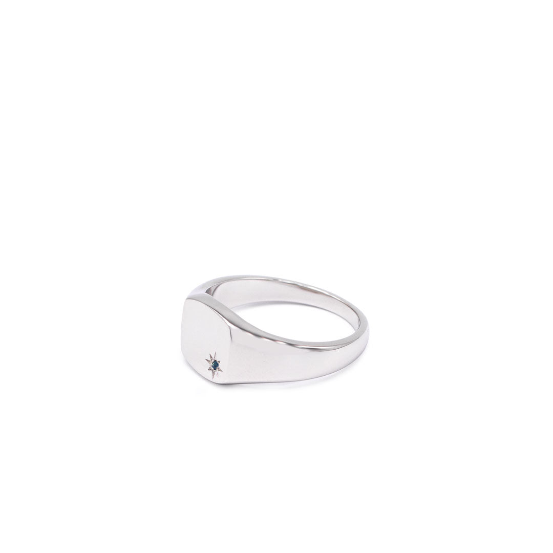 Silver signet ring with rhodium plating, with a star setting and Sapphire stone in the bottom corner on a white background