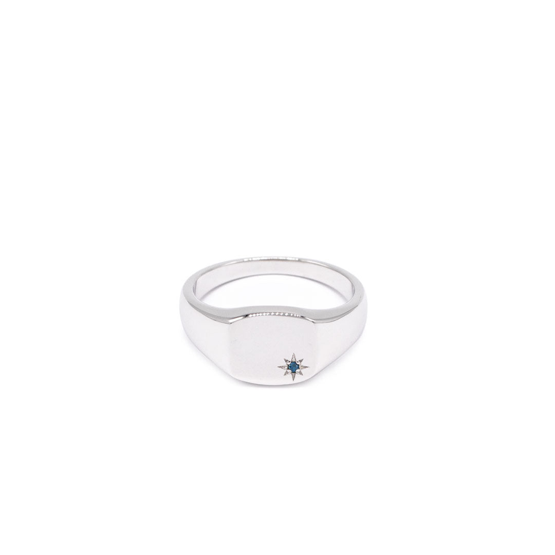 Silver signet ring with rhodium plating, with a star setting and Sapphire stone in the bottom corner on a white background