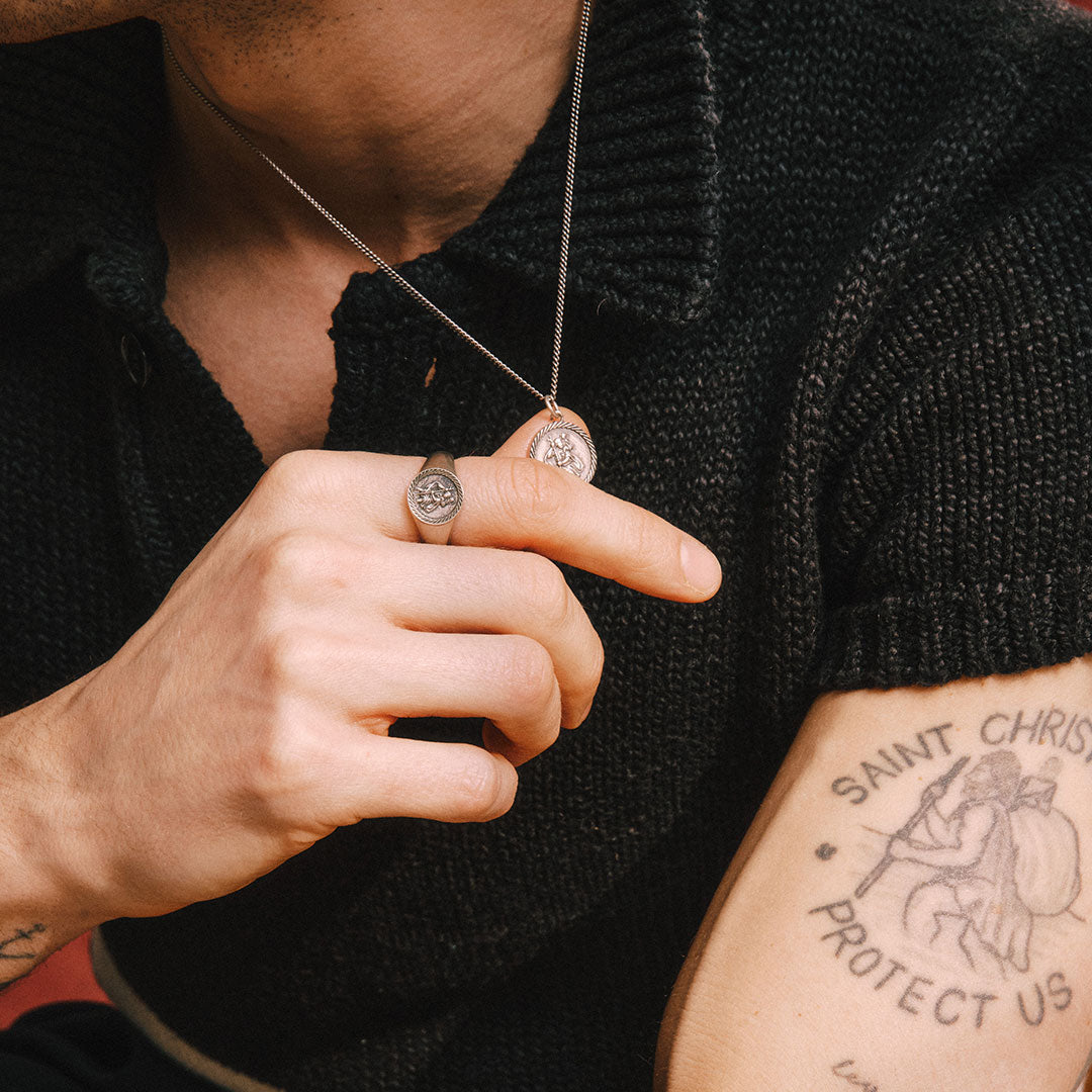 model wears black knitted top while wearing a ring and matching necklace with St Christopher motifs - Serge DeNimes